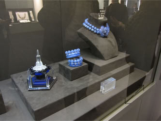 Basel Display Case A display case with blue jewelry, including a necklace, bracelet, and ring, arranged on black stands.