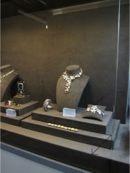 Basel Display Case A glass display case containing various pieces of jewelry, including necklaces and rings, with people visible in the background design of the trade show booth and displays by Swiss Packaging of New York and Switzerland