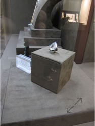 Basel Display Case A large diamond displayed on a gray pedestal with a reflective surface, surrounded by other display elements in a museum setting.