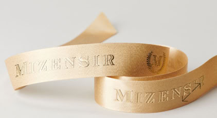 A beige satin ribbon with embossed text and a small emblem by Swiss Packaging of New York and Switzerland