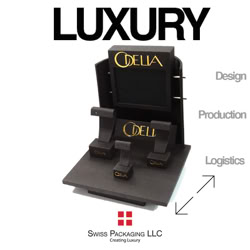 A Brown display stand with the word "Odella" in gold, featuring stands for items. The words "Luxury," "Design," "Production," and "Logistics" are visible, along with a logo and "Swiss Packaging LLC" at the bottom manufactured by Swiss Packaging of New York and Switzerland