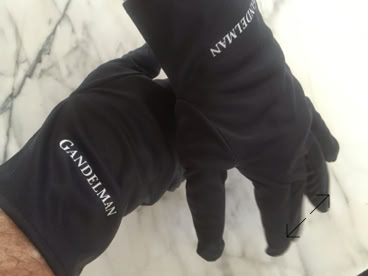 Two hands wearing black jewelers gloves with white text on a marble surface manufactured by Swiss Packaging of New York and Switzerland