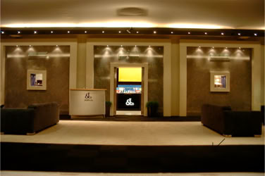 A Basel Watch and Jewlery Fair spacious lobby area with two dark sofas facing each other, a reception desk on the left, framed pictures on the walls, and a central doorway with a lit wall inside design and design by Swiss Packaging of New York and Switzerland