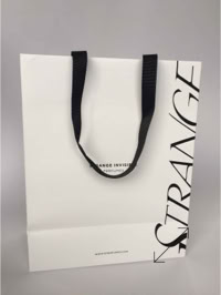 A white shopping bag with black handles and the word "STRANGE" printed vertically on the side created by Swiss Packaging