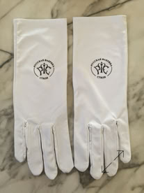 A pair of white Jewelers gloves with a circular logo featuring text, placed on a marble surface manufactured by Swiss Packaging of New York and Switzerland