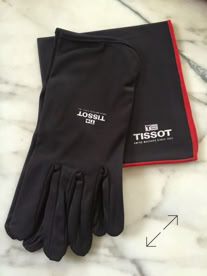 Black jewelers gloves with "Tissot" branding placed on a black and red polishing cloth, on a marble surface manufactured by Swiss Packaging of New York and Switzerland