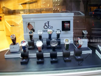 A Jacob & Co. watch display case with multiple wristwatches on stands, set against a backdrop with a logo and text design by Swiss Packaging of New York and Switzerland
