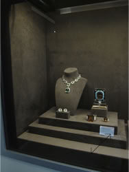 Basel Display Case A glass display case containing various pieces of jewelry, including necklaces and rings, with people visible in the background design of the trade show booth and displays by Swiss Packaging of New York and Switzerland
