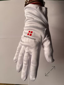 A white jewelers glove with a red Swiss Packaging logo and text on the back, worn on a hand against a plain background manufactured by Swiss Packaging of New York and Switzerland
